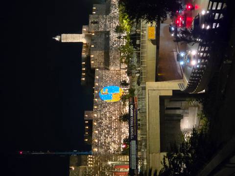 Nighttime city walls of Jerusalem lit with projected artwork above a busy road with car light trails.