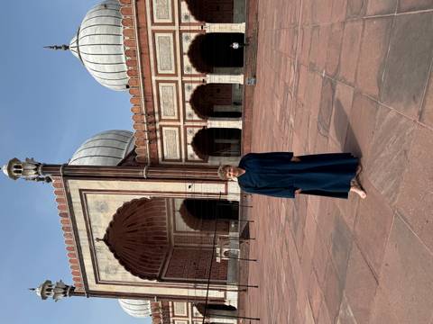 Portrait-oriented shot of woman in blue cloak standing barefoot in Jama Masjid courtyard.