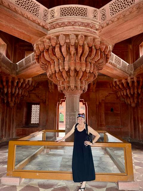 Smiling traveller poses beneath intricately carved central pillar inside Fatehpur Sikri's Diwan-i-Khas.