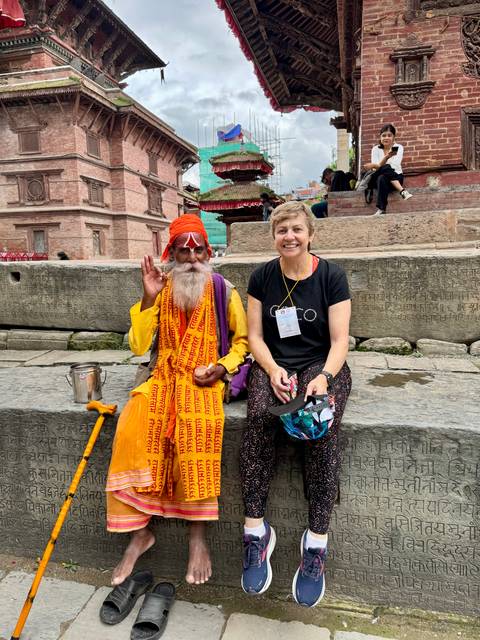 Tourist sits with a colourfully dressed sadhu on carved stone steps of Patan Durbar Square.