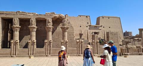 Travelers explore an ancient sandstone temple courtyard with tall columns and blue desert sky.