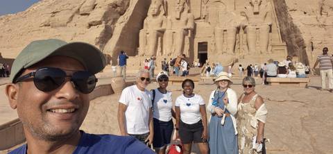Smiling tour group posing for a selfie in front of the colossal statues of Abu Simbel.