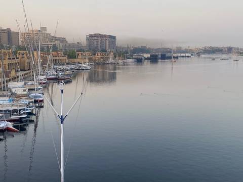 Calm morning view of a Nile riverside city with moored boats and hazy skyline.