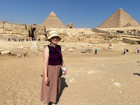 Traveler in sunhat standing in front of the Great Pyramids and Sphinx on a sandy plateau.