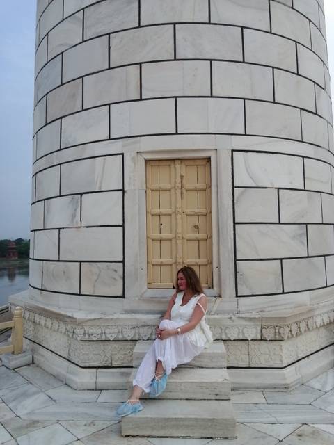 Woman seated beside a marble tower segment of the Taj Mahal overlooking the river.