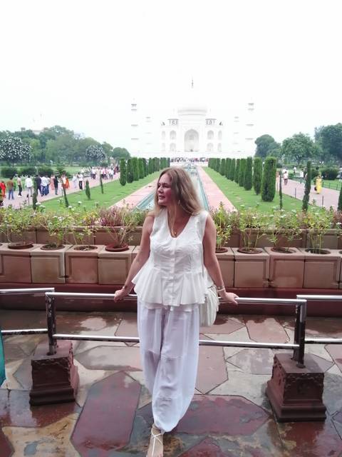 Woman posing on terrace with long water channel and Taj Mahal in the distance.