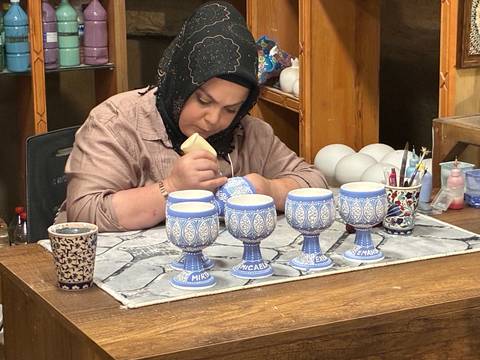 A craftswoman carefully hand-paints ornate blue goblets in a pottery workshop.