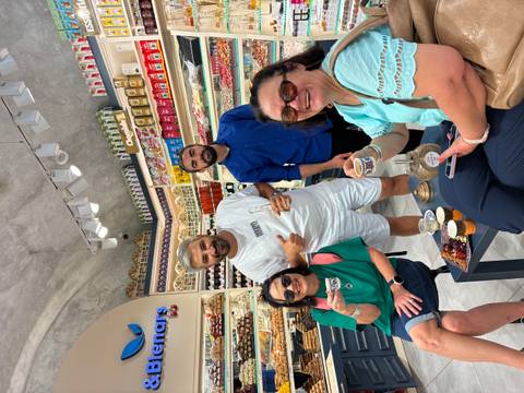 Travelers sample Turkish delights inside a brightly lit sweet shop lined with shelves of confections.