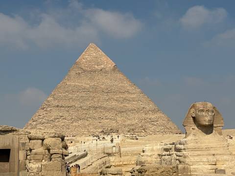 Great Pyramid of Giza rises against blue sky with the Sphinx in the foreground.