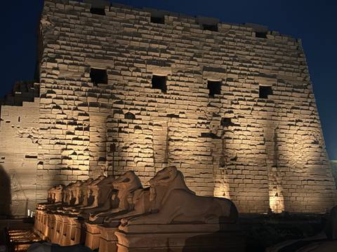 Night lighting bathes ram-headed sphinx statues and massive stone walls of Luxor Temple.