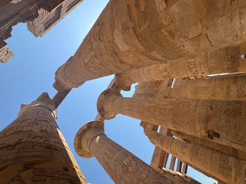 Upward view of colossal hieroglyph-carved columns of Karnak Temple against a bright blue sky.