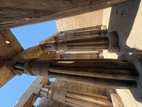Massive stone papyrus columns of an ancient temple captured from ground level with clear sky above.