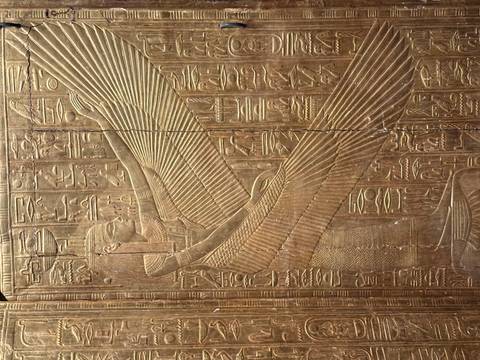 Golden relief panel depicting the winged goddess Isis surrounded by dense hieroglyphs.