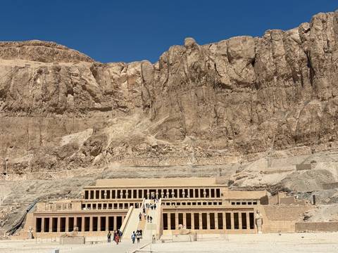 Temple of Hatshepsut nestles against towering limestone cliffs under a deep blue sky.