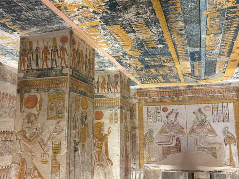 Vividly painted tomb chamber with intricate ceiling and column murals depicting Egyptian deities.