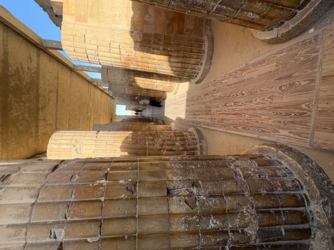 Narrow corridor of Saqqara’s Step Pyramid complex lined with fluted stone columns and a wooden walkway.