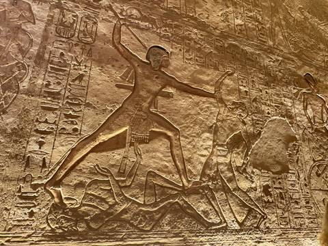 Relief of Pharaoh trampling enemies on a sunlit carved stone wall rich with hieroglyphs.