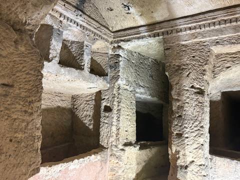 Rough-hewn rock chambers and niches inside an ancient tomb or catacomb lit by soft light.