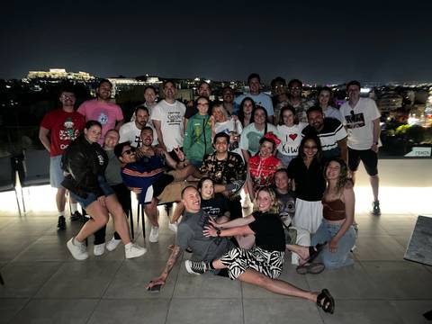 Large tour group posing on a rooftop terrace at night with the illuminated Acropolis visible in the distance.