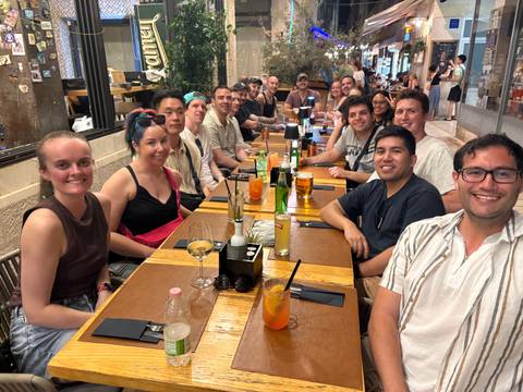 Long table of travellers sharing food and drinks inside a cosy restaurant setting.