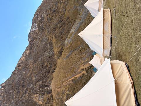 Series of cream canvas bell tents pitched on grassy terrain beneath rugged mountain slopes.