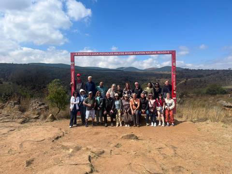Large tour group poses under a red frame sign at Bourke’s Luck Potholes viewpoint.