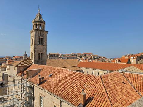 Sunny rooftop panorama of Dubrovnik with a prominent church bell tower against blue sky.