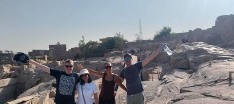 Four smiling travellers pose with arms raised amid sun-lit ancient stone ruins.