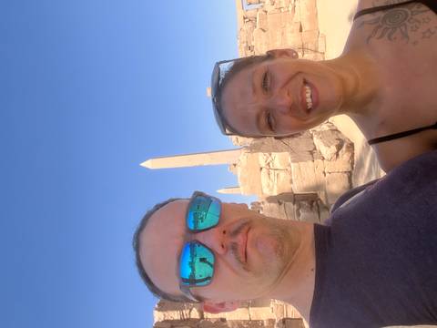 Couple stands before ancient sandstone obelisks under a cloudless blue sky.