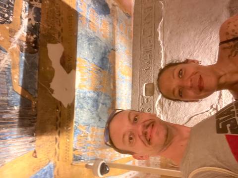 Couple inside a richly painted ancient tomb chamber with colourful hieroglyphic ceiling.