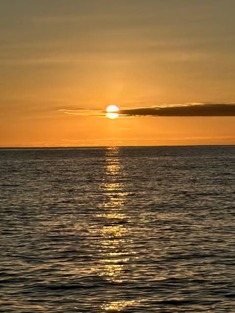 Golden sun sets over a calm ocean, casting a shimmering reflection on the water.