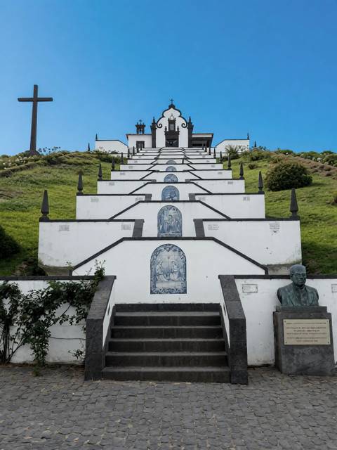 White zig-zag staircase decorated with blue tile panels climbing to a hilltop chapel.