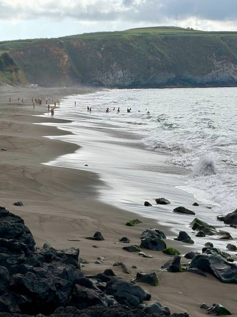 Wide sandy beach with gentle waves and scattered swimmers along the shoreline.