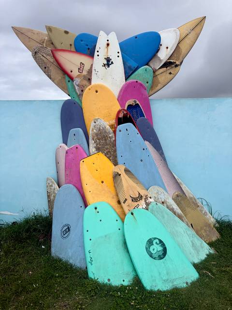 Colorful stack of old surfboards arranged as a sculpture against a blue wall.