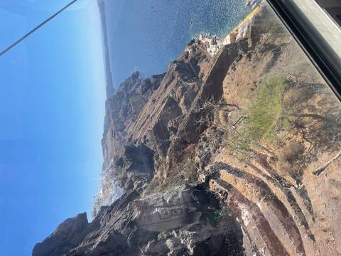 View through a gondola window of steep volcanic cliffs dropping into the deep blue Aegean Sea in Santorini.