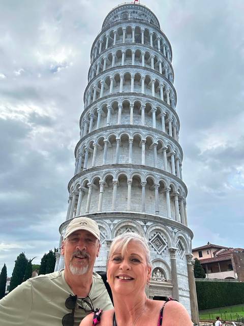 Traveler poses humorously in front of the Leaning Tower of Pisa under a cloudy sky.