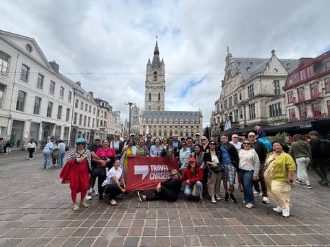 Tour group holding a red flag in a European square with a tall medieval belfry in the background.