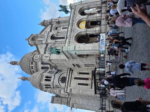 Crowds gather before the domes and stone arches of the Sacré-Cœur Basilica on Montmartre.
