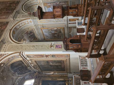 Richly decorated baroque church interior with frescoed ceilings, carved wood pulpit and benches.