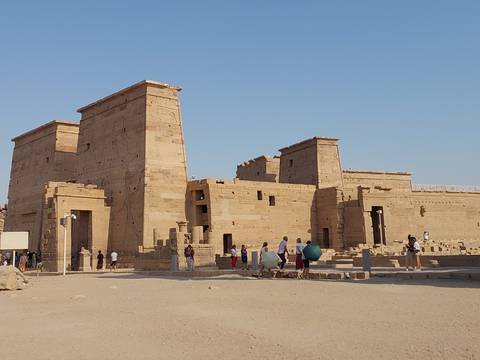 Visitors exploring the sandy courtyard of the ancient Philae Temple under a clear sky.