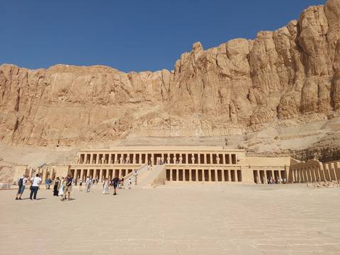 Temple of Hatshepsut set against towering desert cliffs with visitors on the broad courtyard.