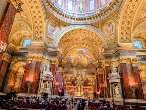 Opulent basilica interior with gilded columns, domed ceiling and chandeliers