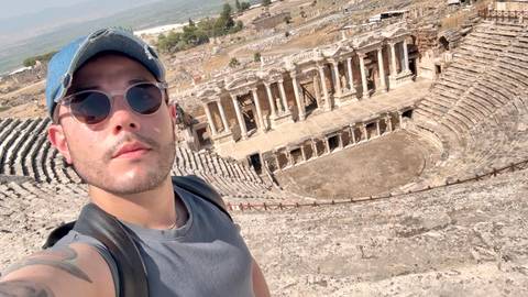 Selfie of a traveler at the ancient stone amphitheater of Hierapolis overlooking the stage and seating tiers.