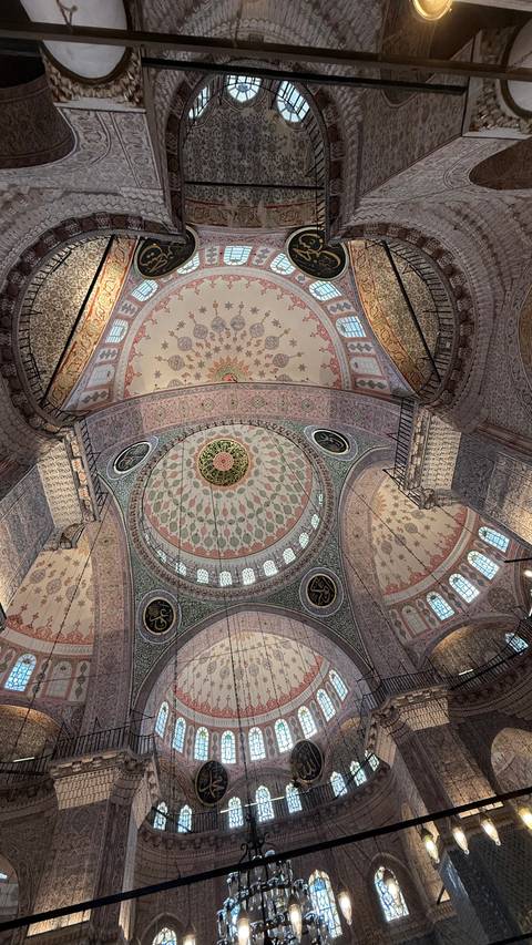 Ornate domed ceiling of an Ottoman mosque with intricate floral and geometric tile designs and calligraphy.
