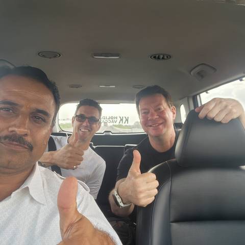Happy passengers give thumbs-up while riding in the back seat of a car during an Indian road trip.