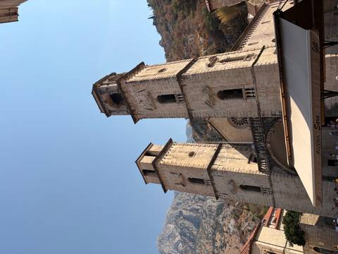 Twin stone bell towers of a historic cathedral stand against a clear blue sky and mountain backdrop.