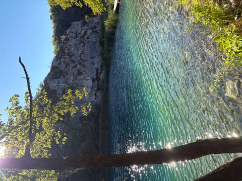 Crystal-clear turquoise lake framed by rocky cliff walls and sunlit foliage.