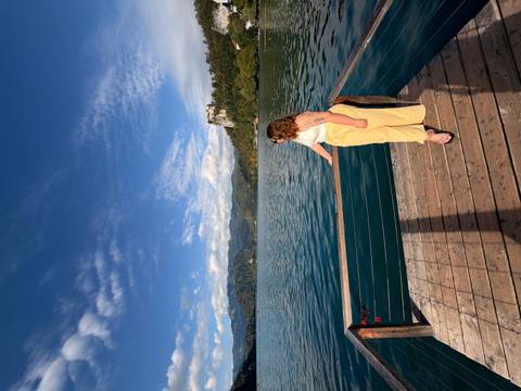 Woman on a wooden pier gazes over Lake Bled with Bled Castle perched on a forested hill.