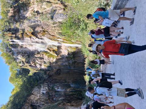 Crowd of visitors in front of a high cascading waterfall within a lush national park.