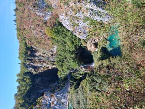 Panoramic view of tiered waterfalls, turquoise pools and dense greenery in a canyon.